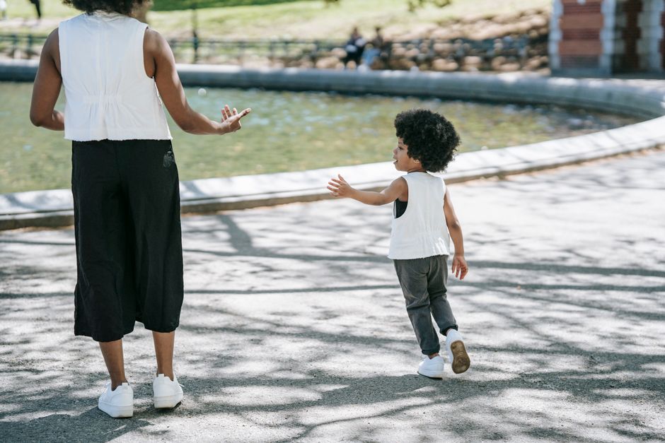 A mother and daughter walking in the park on a sunny day in matching outfits.