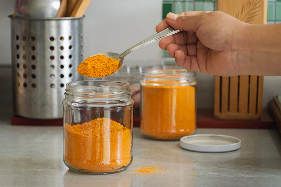 A close-up of turmeric powder being scooped into a jar in a kitchen with utensils.