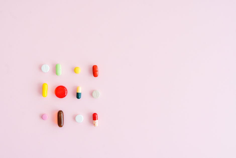 Colorful assortment of pills and capsules arranged on a pastel pink background, perfect for healthcare themes.