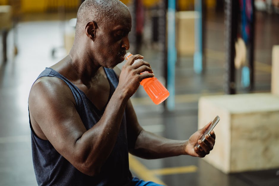 African American man in gym drinking sports drink while using smartphone. Fitness and connectivity concept.