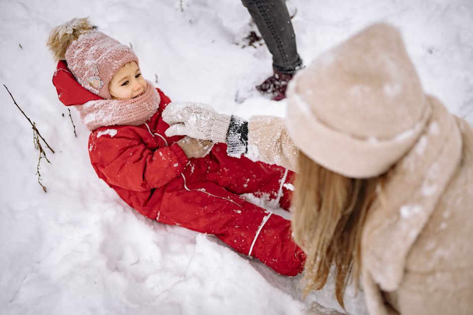 Child in a red snowsuit playing in the snow with an adult