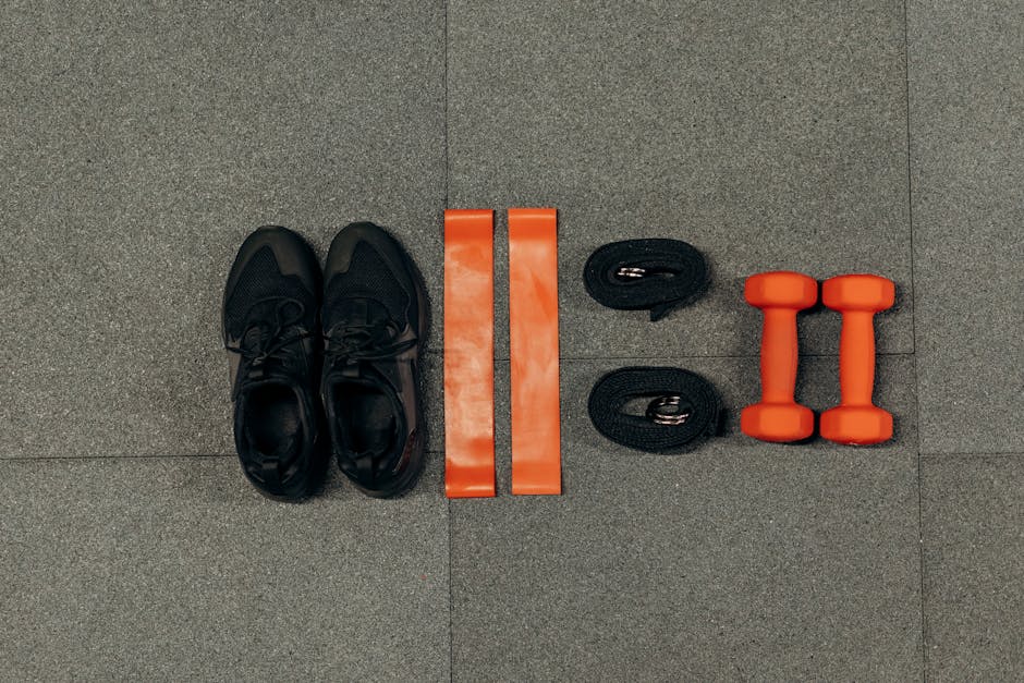 Flat lay of gym essentials including dumbbells, sneakers, and resistance bands on a grey floor.