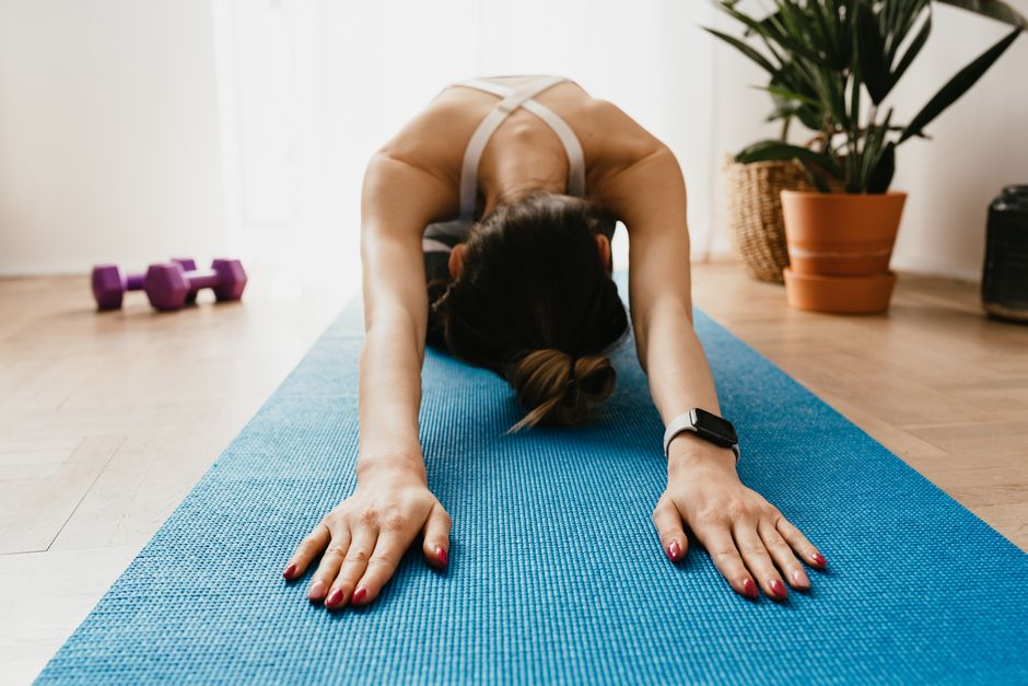 Full body faceless fit female wearing smartwatch stretching body in Child Pose on blue mat