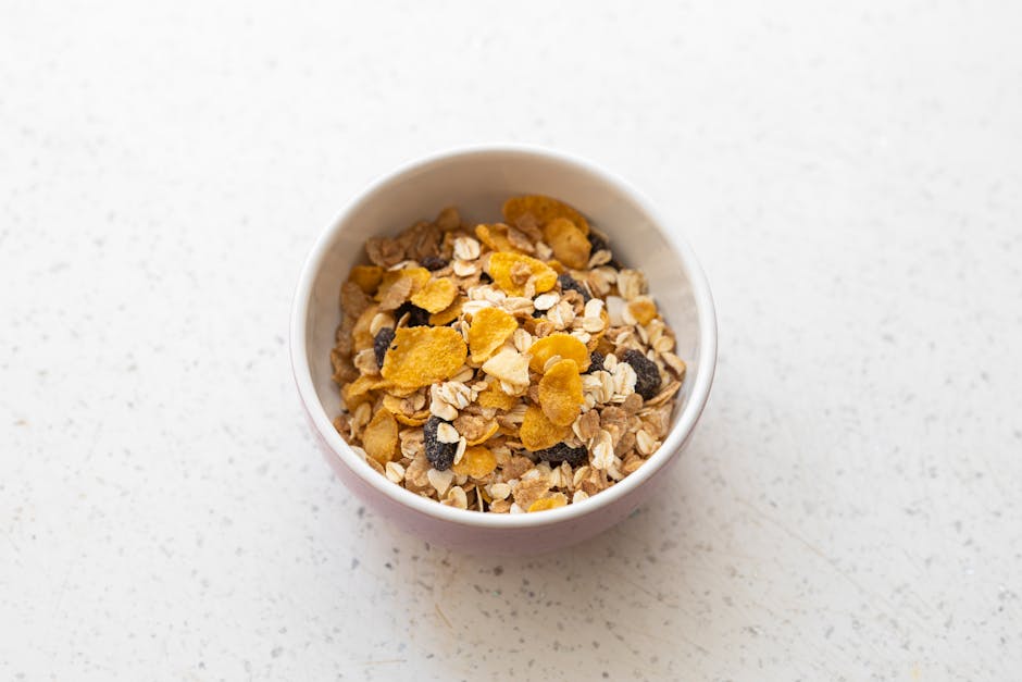 A ceramic bowl filled with mixed cereals including cornflakes, oats, and raisins on a white surface.