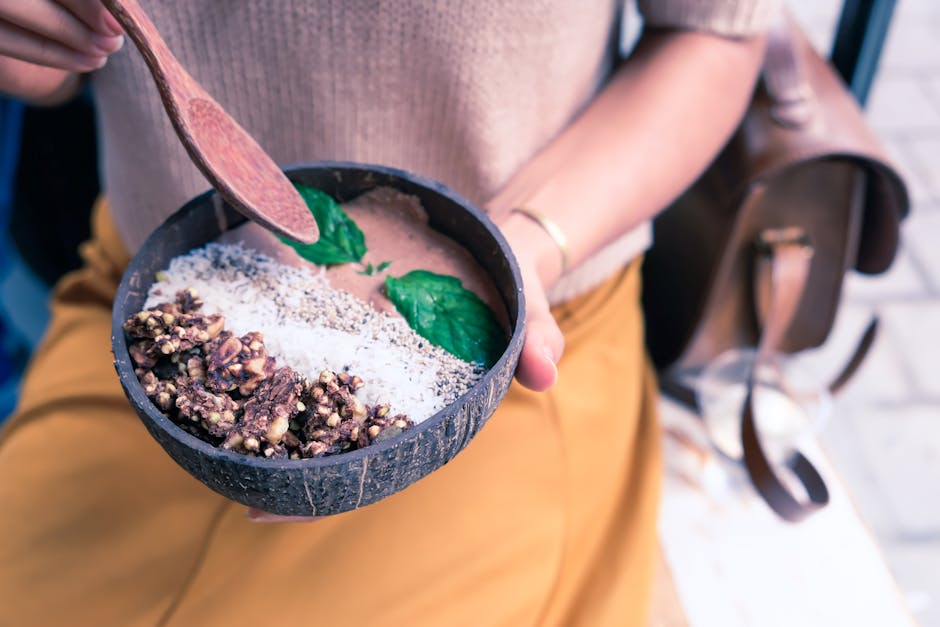 A nutritious breakfast bowl held by a woman, featuring granola, seeds, and mint leaves for a healthy start.
