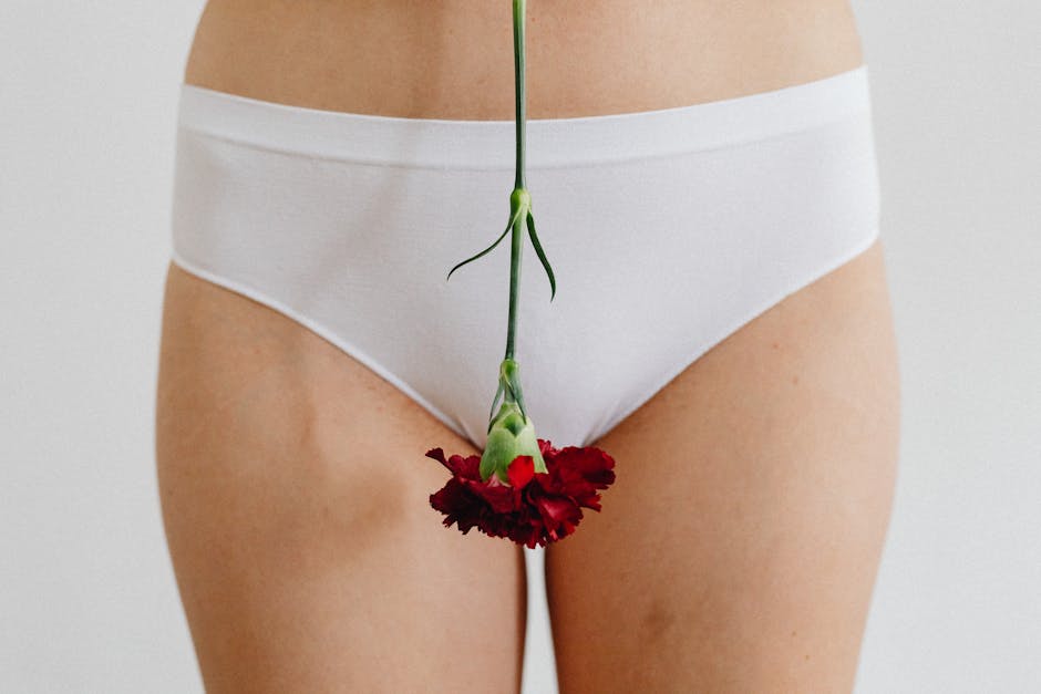 Close-up of woman's hips in white panties holding a red flower, symbolizing femininity and menstruation.