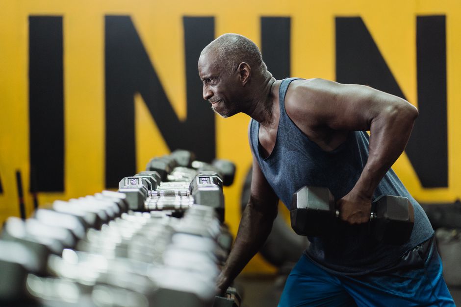 Strong senior man focusing on strength training with dumbbells in a vibrant gym.