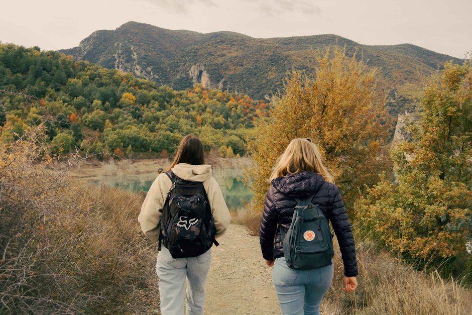 Two hikers with backpacks walking toward the hills on a trail
