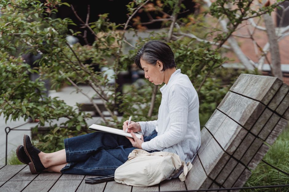 Woman sitting outdoors on a bench writing in a notebook
