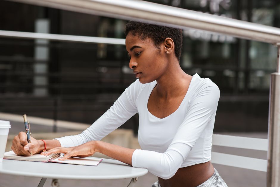 Woman writing in a notebook at a table on a balcony